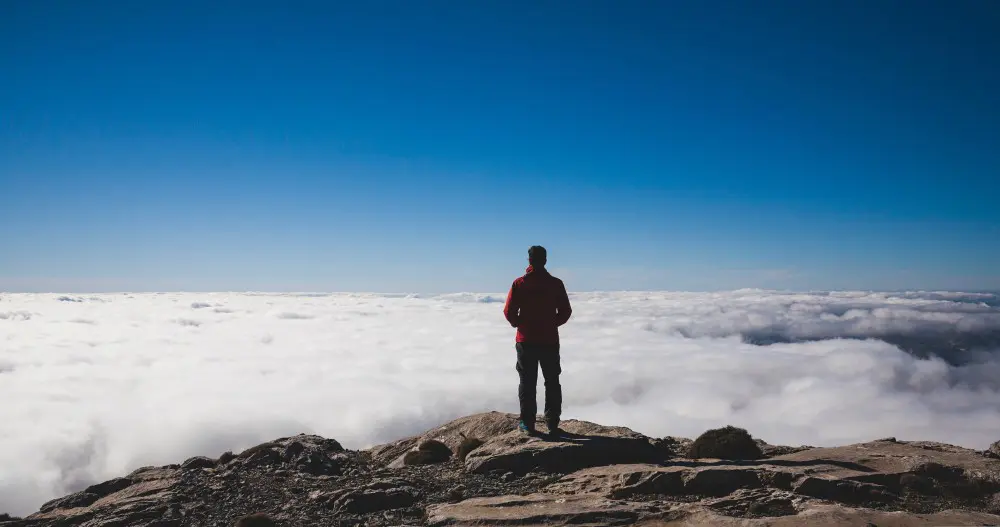 man on a mountain looking at clouds