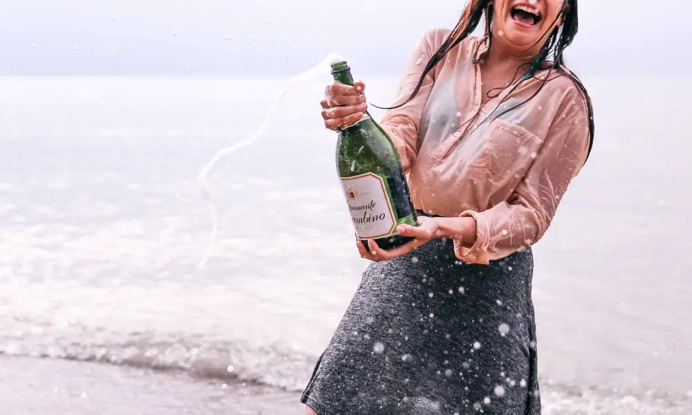 woman popping champagne on a beach