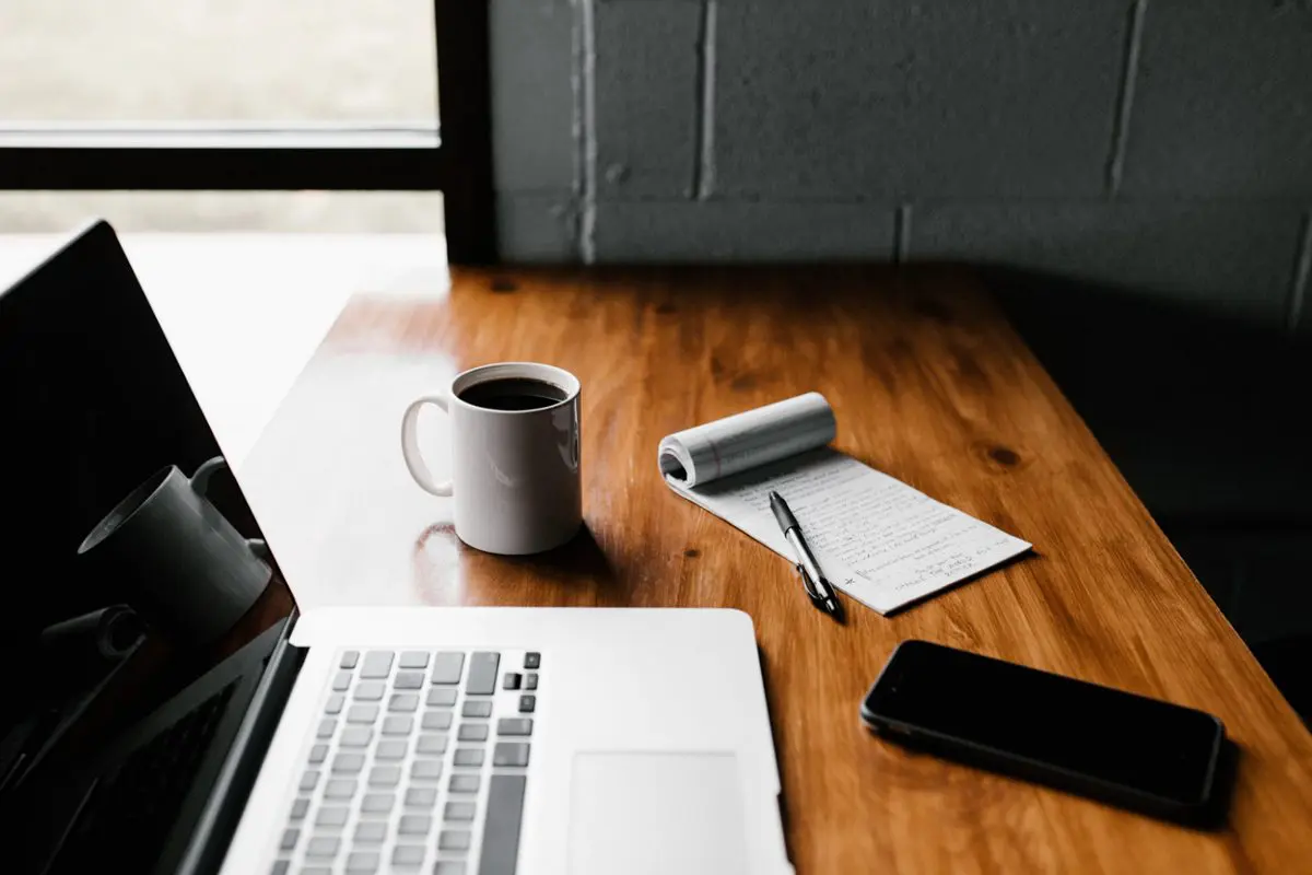 Checklist, laptop, coffee, and phone on a table